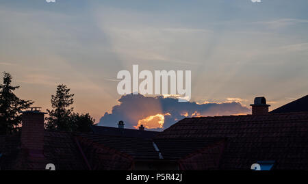 Lever de soleil dans la ville avec des toits et cloud holey derrière les arbres. Banque D'Images