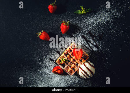 Gaufres Belges avec de la crème glacée et les fraises sur un fond noir. Banque D'Images