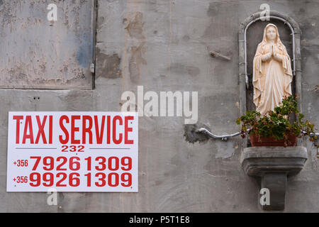 Signer une publicité à côté de taxi d'une statue de la Vierge Marie sur un mur à Gozo, Malte. Banque D'Images