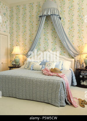 Coronet avec rideaux bleu au-dessus de lit king size dans la chambre avec un papier peint fleuri vert et lampes allumées Banque D'Images