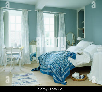 Blanc +bleu et blanc jeter oreillers sur lit dans chambre bleue avec voile rideaux et volets peints sur windows Banque D'Images