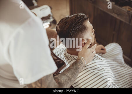 Coiffure lubrifie la barbe du client avec de l'huile. Photo en style vintage Banque D'Images