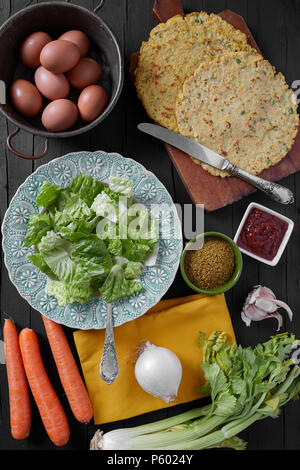 Vegan crêpes avec les oeufs, les carottes, le céleri, les oignons, l'ail et les épices. Vue de dessus tourné sur fond de bois noir. Banque D'Images