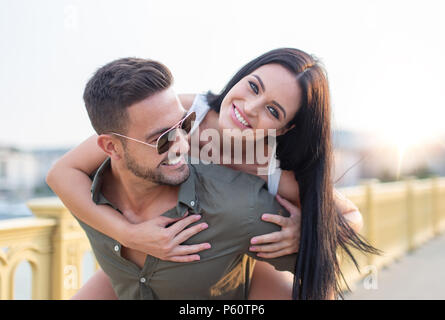 Happy young woman piggyback sur l'homme élégant en plein air
