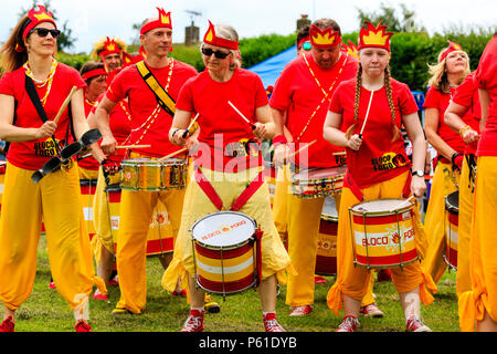 Fogo Bloco Sambra Drumming Bande, à Custard Pie Championship, Coxhealth. Vêtus de rouge et jaune, la rangée de batteurs face. Banque D'Images