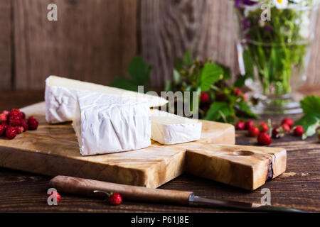 Fromage brie française, les fraises des bois et blanc bouquet de fleurs sauvages mauves sur table en bois en milieu rural Banque D'Images