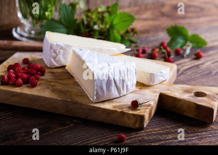 Fromage brie française, les fraises des bois et blanc bouquet de fleurs sauvages mauves sur table en bois en milieu rural Banque D'Images