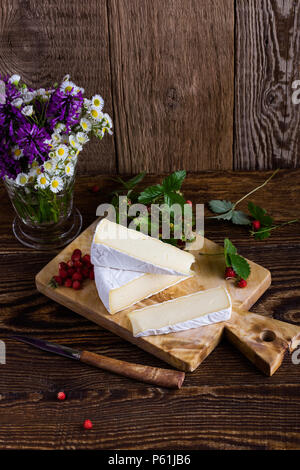 Fromage brie française, les fraises des bois et blanc bouquet de fleurs sauvages mauves sur table en bois en milieu rural Banque D'Images