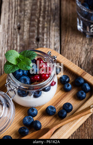 Les parfaits crème Cheesecake aux myrtilles et petits fruits groseille rouge servi dans un pot, sans cuisson d'été délicieux dessert sur la table rustique en bois prêt à manger Banque D'Images