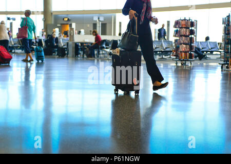 Vue de personnes, d'une femme, à partir du cou, faisant leur chemin dans un terminal de l'aéroport avec un sol réfléchissant, tirant une assurance vers et depuis le Banque D'Images