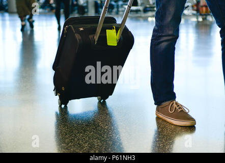 Vue d'un homme vêtu de jean jambes à faire leur chemin à travers un terminal de l'aéroport avec un sol réfléchissant, tirant de bagages à rouleaux et de la compagnie aérienne Banque D'Images