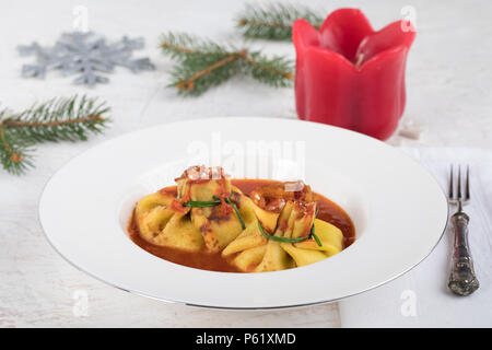 Boulangerie italienne pâtes fagottini, rempli de fromage ricotta, et la serrer avec de la ciboulette fraîche sur la sauce tomate, le plat typique de l'hiver, les vacances en Italie. Banque D'Images