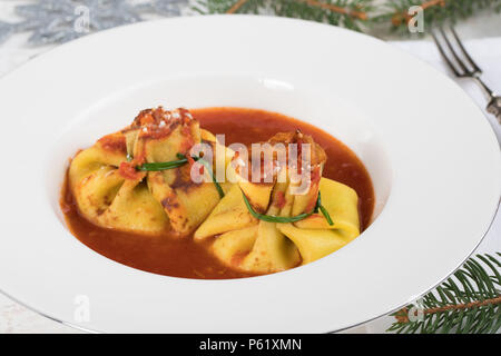 Pâtes fagottini au four rempli de fromage ricotta et serré avec la ciboulette, sur lit de sauce tomate, la plaque de la cuisine italienne traditionnelle. Banque D'Images