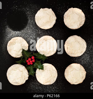 Petits pâtés de Noël fraîchement cuits au four avec un manque, avec Holly berry branche feuilles et sucre glace Poussière sur fond noir. Vue d'en haut. Banque D'Images