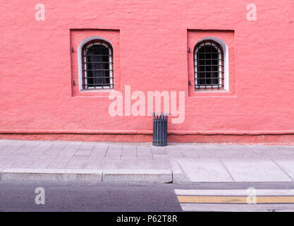 Mur peint en rouge avec fenêtre en treillis et poubelle près du trottoir, l'architecture de base. Banque D'Images