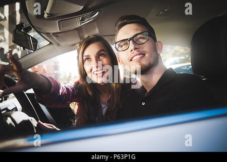 Profitant de voyage. Beau jeune couple assis sur les sièges passager avant et souriant tout en bel homme conduisant une voiture. Banque D'Images