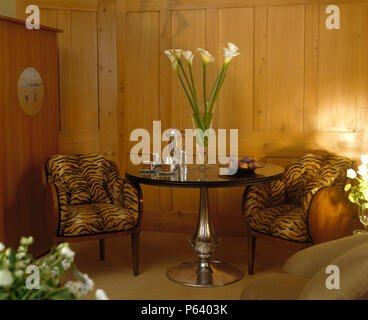 Impression de tigre années 30 chaises capitonnées metglass surmontée al table avec vase d'arums blancs dans un salon lambrissé de pin Banque D'Images