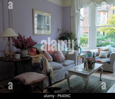 Table à café peint en face du bar rayé canapé avec coussins empilés dans maison mauve salon avec baie vitrée Banque D'Images