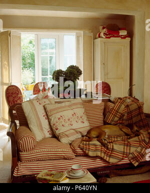 Couchage chien le checked couverture sur canapé Bergère et coussins à rayures florales dans salon cottage Banque D'Images