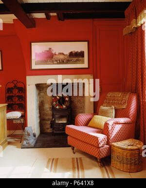 Fauteuil rouge à motifs à côté de cuisinière dans une cheminée dans un salon rouge Banque D'Images