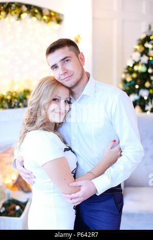 Young woman hugging homme portant une chemise blanche, décorée pour Noël en arrière-plan. Banque D'Images