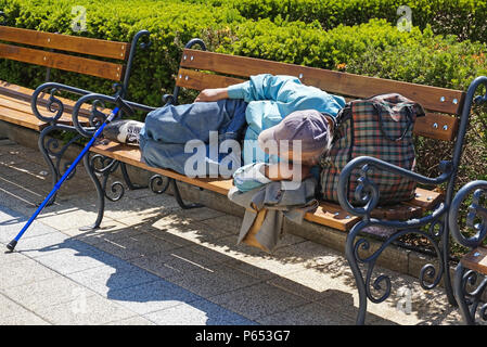 Sans-abri est en train de dormir sur un banc de parc piscine Banque D'Images