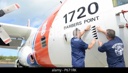 U.S. Coast Guard le Cmdr. Jeffrey Jager, officier des opérations de la Garde côtière pour Air Station barbiers Point, et David Schofield, National Oceanic and Atmospheric Administration et la santé des mammifères marins, gestionnaire du Programme d'intervention pré-positionner le phoque moine Hawaiien sept autocollants sur un avion Hercules HC 130 à Air Station Point, New York, barbiers 16 mai 2016. La NOAA a présenté le phoque moine Hawaiien de décalcomanies pour Air Station barbiers équipage Point en reconnaissance de leur importante contribution à la conservation du phoque moine Hawaiien programme. (U.S. Photo de la Garde côtière du Maître de 2e classe Tara Molle) Banque D'Images