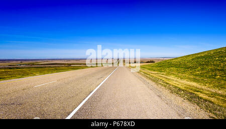Panorama d'une longue route asphaltée entre les champs avec de l'herbe bien verte, un ciel bleu, un jour d'été Banque D'Images