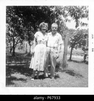 Photographie noir et blanc, montrant un couple plus âgé, tous deux souriant, debout à l'extérieur dans toute la longueur, l'homme porte une chemise et un pantalon de couleur claire, et s'enroule son bras autour de la taille de sa femme qui porte une lumière colorée, thé-longueur robe, avec le feuillage en arrière-plan, probablement photographié dans l'Ohio, en juin 1956. () Banque D'Images