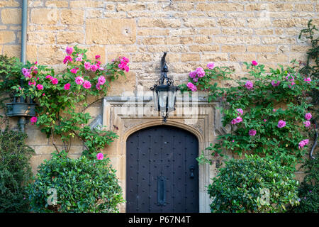 Roses roses autour d'une maison en pierre de Cotswold porte avant dans l'été. Broadway, Cotswolds, Worcestershire, Angleterre. Banque D'Images