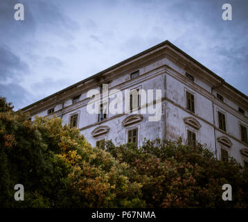 L'angle d'une vieille maison hantée européenne / lost place style avec des fenêtres cassées, entouré d'arbres sous un ciel crépusculaire. Banque D'Images