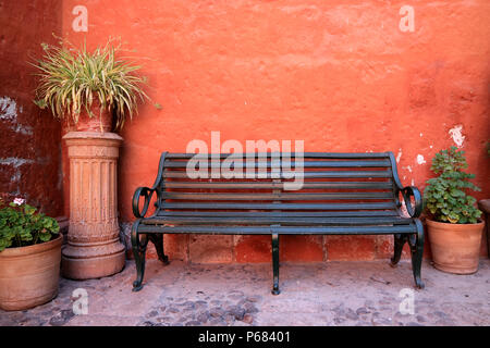 Banc en bois noir en face du mur de couleur orange avec de nombreux planteurs en terre cuite, Monastère de Santa Catalina à Arequipa du Pérou Banque D'Images