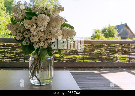 Un bouquet de lilas blanc dans un bocal en verre sur une table sur la véranda d'une maison de village Banque D'Images