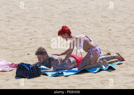 Bournemouth, Dorset, UK. 29 Juin, 2018. Météo France : sunseekers tête à la plages de Bournemouth sur un autre jour ensoleillé chaud avec un ciel bleu et soleil ininterrompue. Une légère brise rend la chaleur plus supportable. Woman rubbing lotion solaire crème sur nos partenaires retour. Credit : Carolyn Jenkins/Alamy Live News Banque D'Images