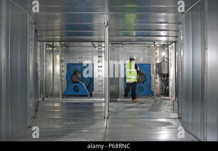 Un ingénieur travaille sur le moteur du ventilateur à l'intérieur d'un conduit d'air conditionné géant au cours de la construction d'un nouveau bâtiment de bureaux à Londres, Royaume-Uni Banque D'Images