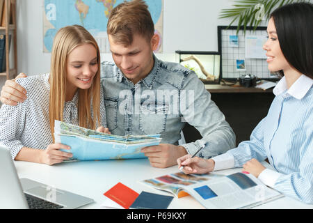 Jeune couple dans une agence de voyages la communication avec un agent de voyage Voyager concept holding brochure Banque D'Images