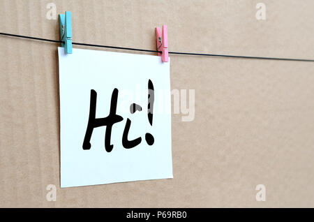Bonjour ! La note est écrite sur un autocollant blanc qui se bloque avec un clothespin sur une corde sur un fond de carton brun . Banque D'Images