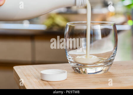 Verser la main le kéfir frais probiotik verre bouteilles en verre transparent, sur une table de cuisine. Banque D'Images