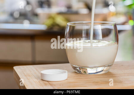 Verser la main le kéfir frais probiotik verre bouteilles en verre transparent, sur une table de cuisine. Banque D'Images