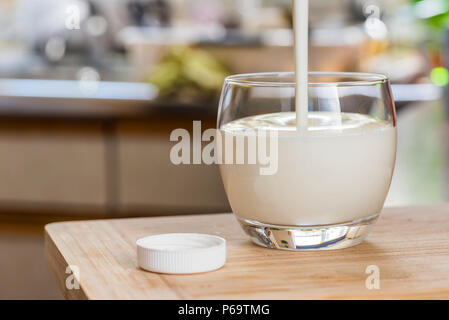 Verser la main le kéfir frais probiotik verre bouteilles en verre transparent, sur une table de cuisine. Banque D'Images