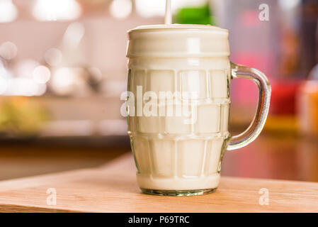 Vue rapprochée versant kéfir frais probiotik verre en verre clair tasse sur une table de cuisine. Banque D'Images