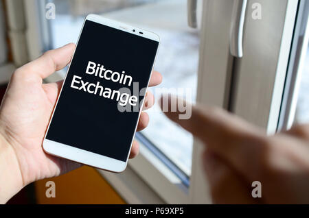 Une personne voit une inscription blanche sur un écran de smartphone noir qui tient dans sa main. Échange Bitcoin . Banque D'Images