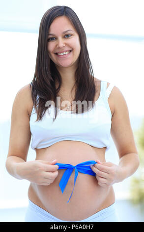 Close up of a smiling pregnant woman attacher un ruban bleu sur son ventre. Banque D'Images