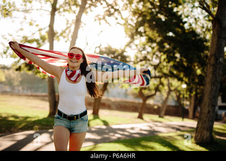 Portrait de femme américaine patriotique fonctionnant sous pavillon national dans le parc et de sourire. Fille dans parc avec USA drapeau en mains la célébration de l'indépendance Banque D'Images