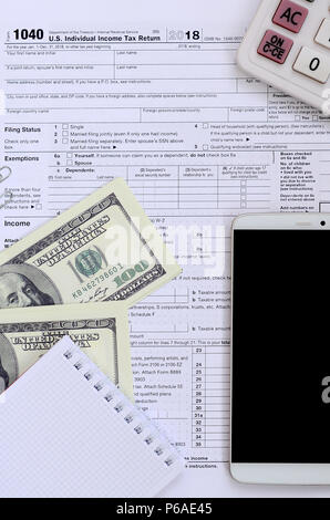 Composition d'articles se trouvant sur le formulaire fiscal 1040. Dollar bills, calculatrice, smartphone, trombone et le bloc-notes. Le temps de payer des impôts . Banque D'Images