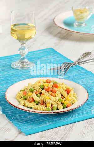 Maison délicieux cuisinés avec des fusillis au pesto de basilic, carottes, maïs et les petits pois dans une assiette sur une serviette bleu turquoise, servi avec un verre de blanc gagner Banque D'Images