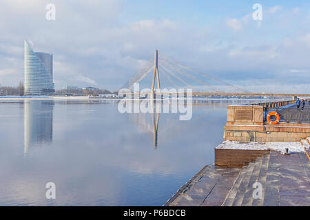 Le remblai de Riga, près de la rivière Daugava dans une froide journée d'hiver dans le contexte d'un gratte-ciel et d'un pont à haubans avec réflexion Banque D'Images