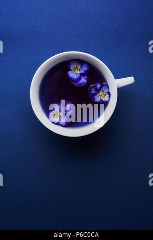 Tasse de thé pois papillon et viola fleurs sur fond bleu Banque D'Images