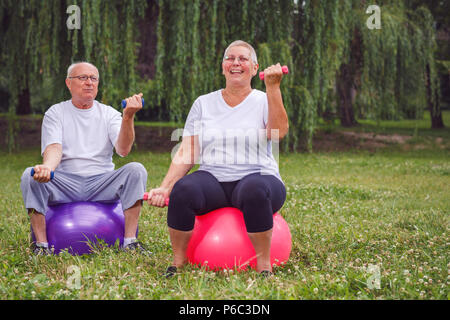 Smiling senior couple holding dumbbells while sitting on exercise ball in park Banque D'Images