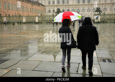 Les touristes avec parapluie dans les couleurs nationales italiennes sur la Piazza Castello, Turin, Italie, avec le Palais Royal derrière. Banque D'Images